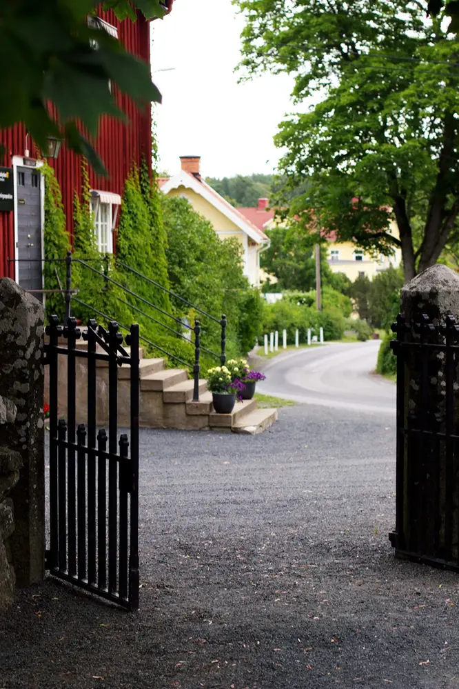 Öppen grind ner mot en en grusgång och gamla hus i olika färger